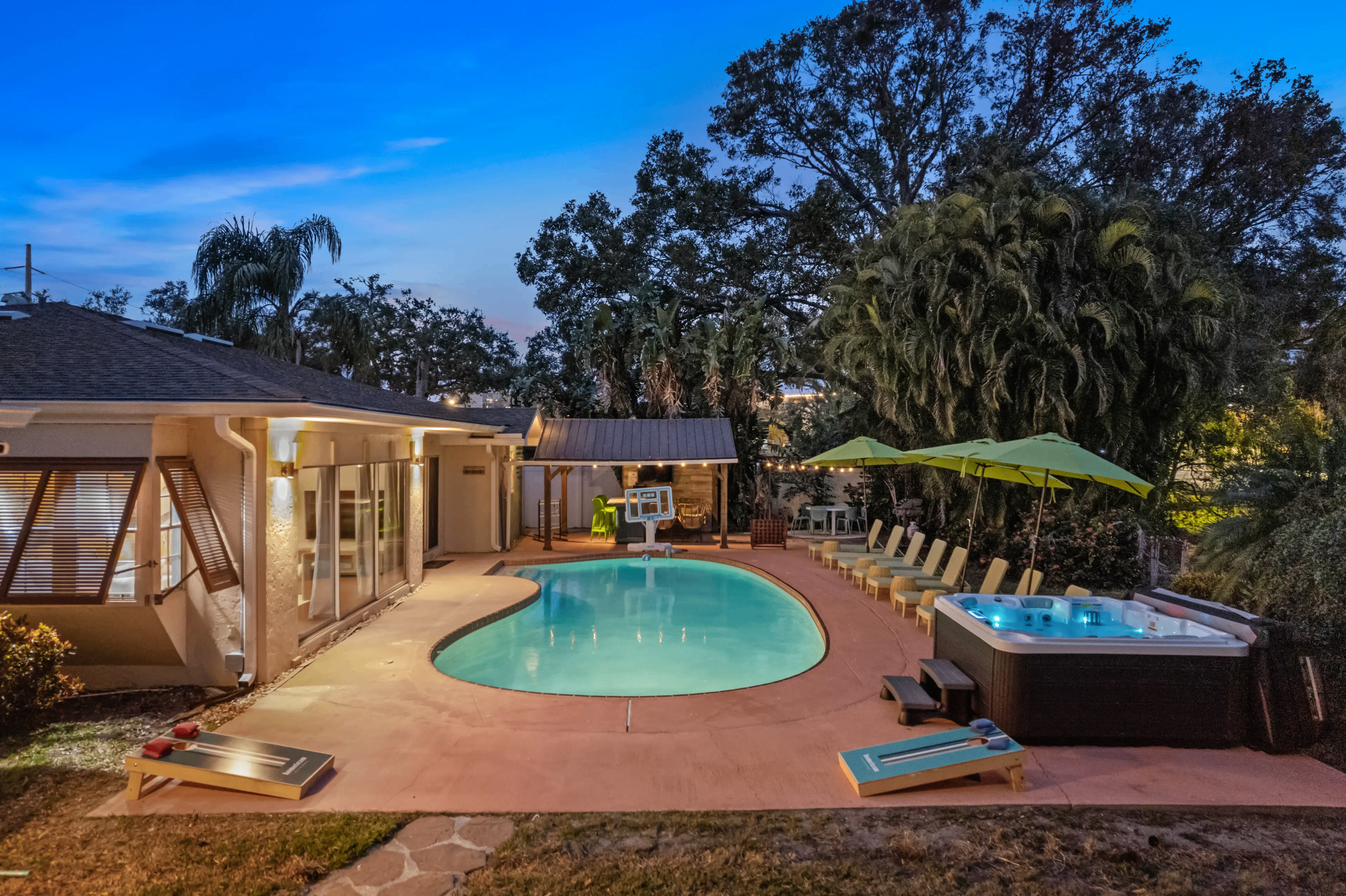 Twilight view of the full backyard oasis — custom pool, hot tub, cabana bar, and lounge deck
