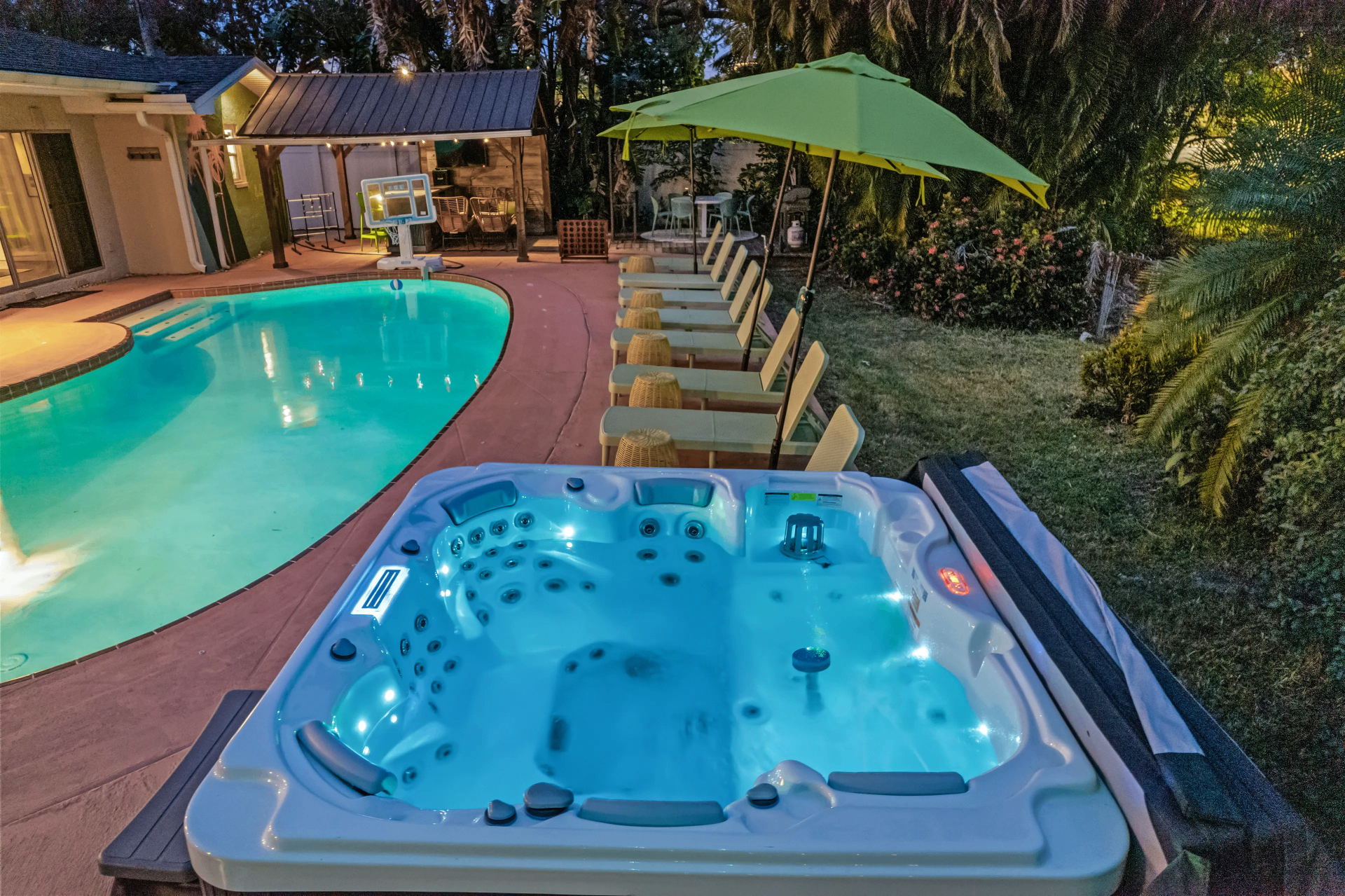 Glowing hot tub beside the lit pool at dusk
